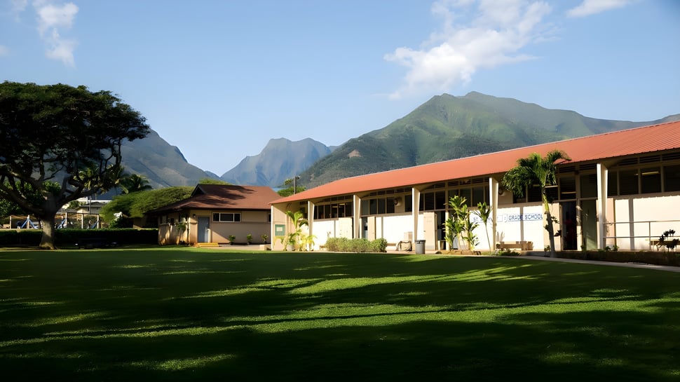 Una pradera verde frente a coloridos edificios con una cordillera de montañas al fondo en el terreno de la St. Anthony School.