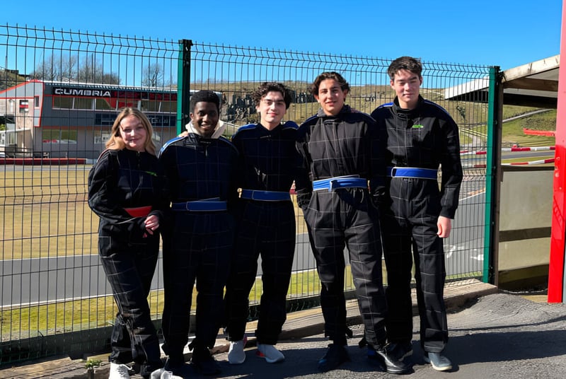 Un grupo de estudiantes en uniformes negros está frente a un área exterior cercada en el campus de la St. Bees School.