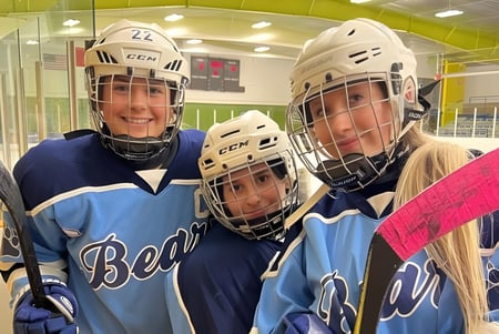 Tres estudiantes de la St. Benedict Catholic Secondary School están con equipo de hockey en una superficie de hielo en la sala de hielo.
