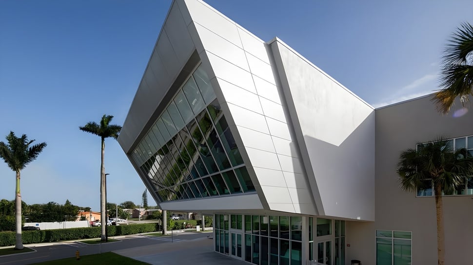 El moderno edificio de la St. Brendan’s Community School con grandes ventanales y palmeras en primer plano bajo un cielo azul.