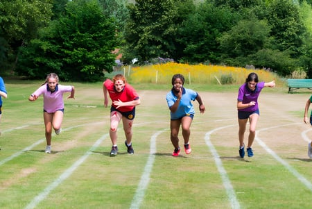 Estudiantes de la St. Catherine's School corren en un campo cubierto de hierba con vegetación verde circundante.