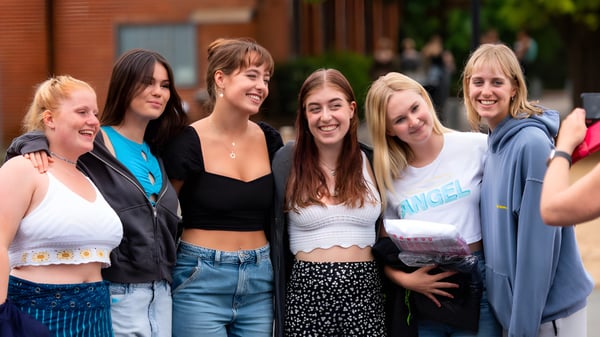 Un grupo de jóvenes estudiantes está riendo juntas en el área exterior de la St. Catherine's School frente a edificios de ladrillo y áreas verdes.