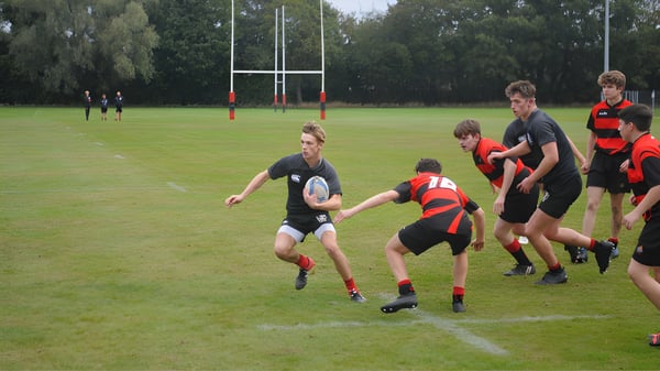 Jugadores de rugby de la St. Christopher School en camisetas rojas y negras juegan en un campo con postes de gol.