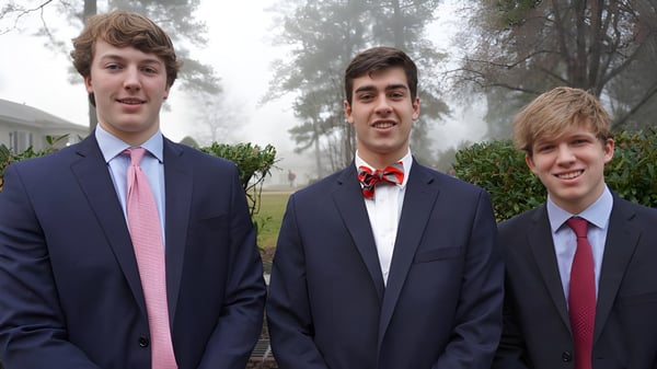 Tres estudiantes de la St. Christopher’s School están juntos al aire libre frente a árboles y áreas verdes.