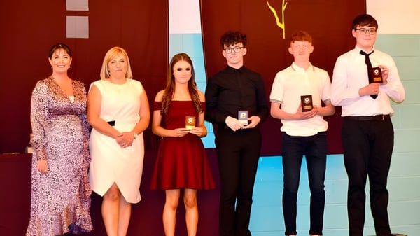 Un grupo de seis personas se encuentra en un evento frente a un fondo colorido en el campus de la St. Ciarán’s Community School.