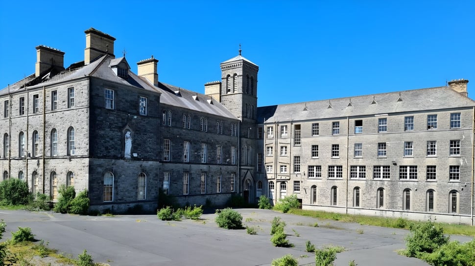 El edificio histórico con varias torres y chimeneas en el campus de St. Coleman's College está rodeado de un paisaje verde.