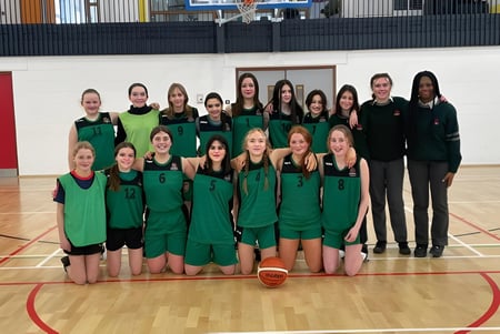 Un grupo de jóvenes jugadoras de baloncesto del St. Colman’s Community College posan juntas en la cancha de baloncesto.