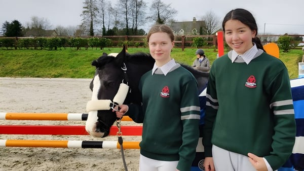 Dos alumnas en uniformes escolares están frente a un caballo en el área exterior del St. Colman’s Community College.