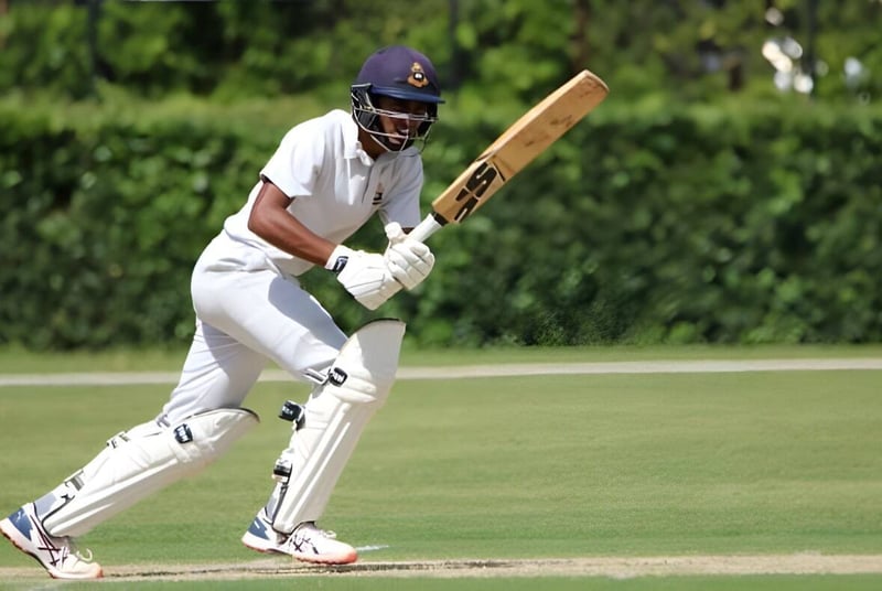 Un jugador de cricket con uniforme blanco sostiene un bate en el campo del St. Columba's College.