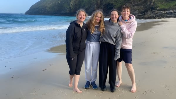 Cuatro alumnas del St. Columba's College están juntas en la playa mirando hacia el mar y los acantilados rocosos.