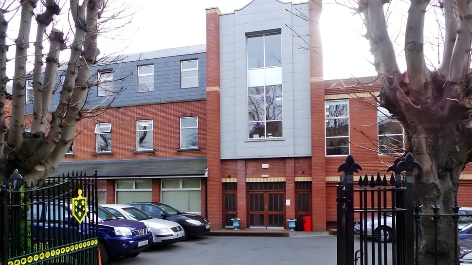 El edificio de St. Conleths College muestra una construcción de ladrillo de varios pisos con una moderna adición de vidrio y árboles desnudos al fondo.