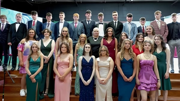 Un gran grupo de estudiantes vestidos formalmente en una ceremonia en St. Cuan’s College se encuentra frente a un escenario.