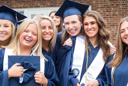 Un grupo de estudiantes de la St. David Catholic Secondary School está en ropa de graduación frente a un edificio de ladrillo celebrando su graduación.