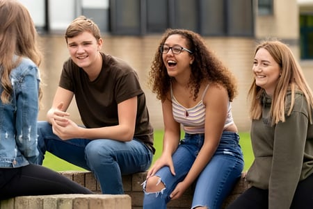 Un grupo de estudiantes se conversa en el área exterior del St. David’s College frente a un edificio con zona verde.