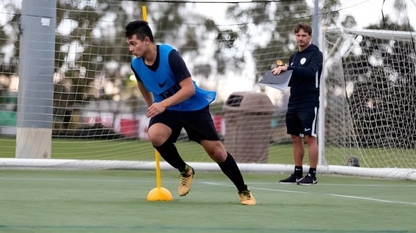 Una estudiante del St. David’s College dribla un balón de fútbol en un campo de césped con otra estudiante al fondo.