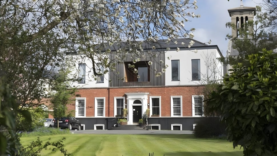 El edificio de St. Dominic’s College con una torre está rodeado de áreas verdes en un césped bien cuidado.