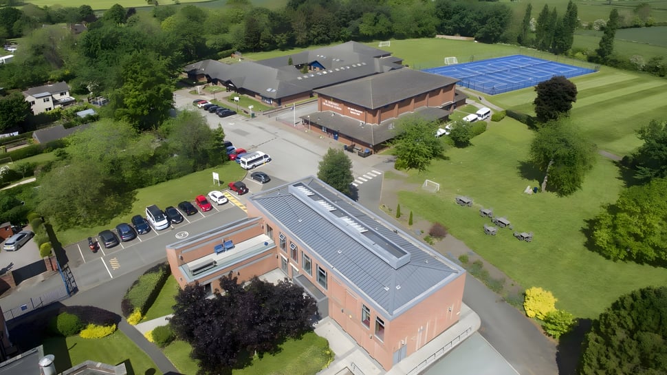 El edificio de ladrillo de varios pisos de la St. Dominic's Grammar School con un sistema de paneles solares azules se encuentra en un prado rodeado de árboles.
