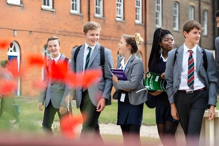 Un grupo de alumnas y alumnos está en el campus de St. Edmund’s College frente a un edificio de ladrillo.