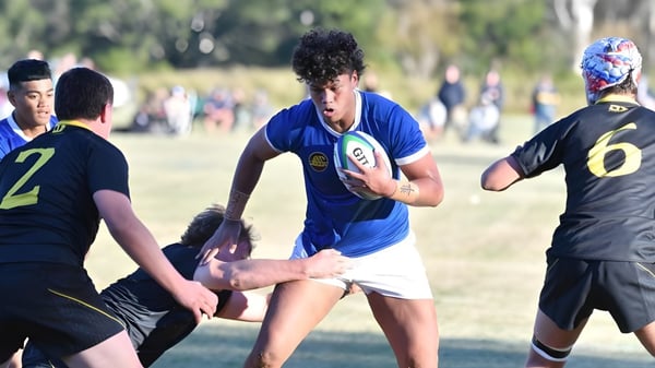 Un grupo de estudiantes juega rugby en el campo de deportes de St. Edmund’s College con árboles y edificios de fondo.