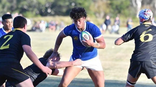 Un grupo de alumnos juega al rugby en el campo de St. Edmund’s College con árboles y edificios al fondo.