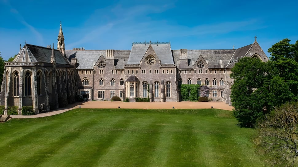 El edificio principal gótico de la St. Edmunds School se encuentra en un césped bien cuidado bajo un cielo despejado.
