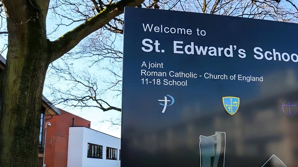 Cartel de bienvenida de la St. Edward's School en Poole con logo de cruz y escudo frente al edificio de ladrillo.