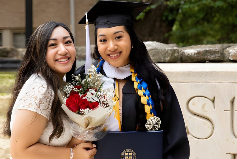 Dos estudiantes de la St Edward's School (Oxford) en togas de graduación se abrazan frente a un edificio universitario.