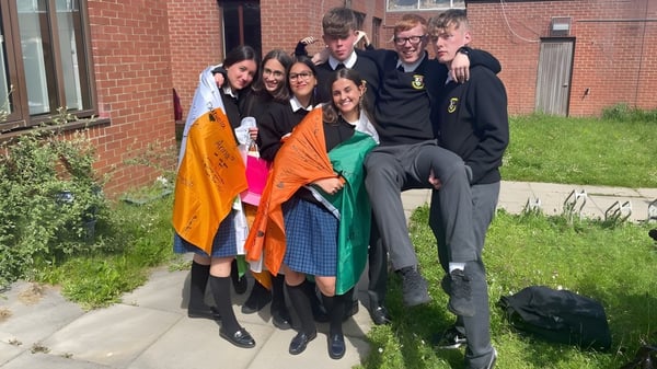 Un grupo de estudiantes está en un prado frente a un edificio de ladrillo en el terreno de St. Finian’s Community College.