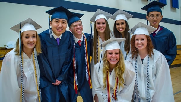 Un grupo de graduadas y graduados de la St. Francis Xavier High School está frente a una pared azul y blanca.