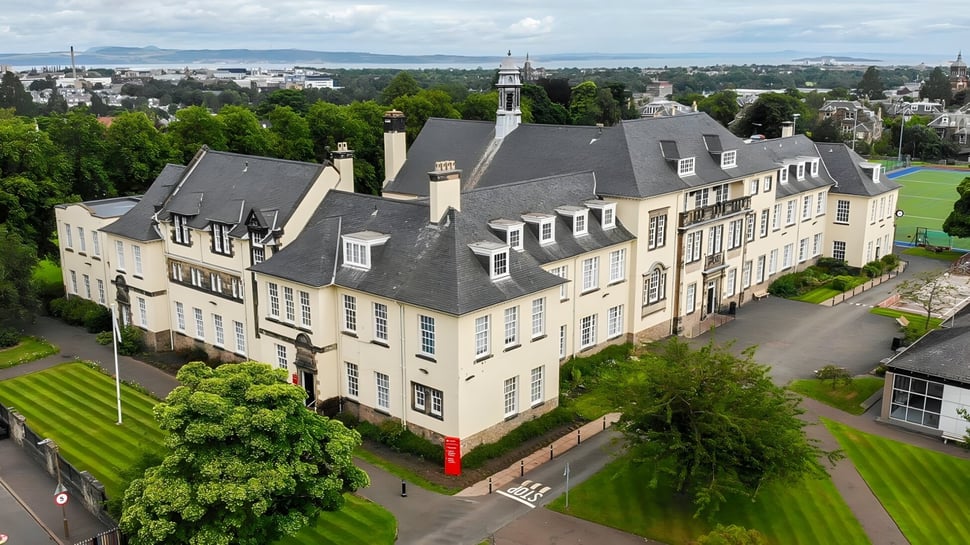El histórico edificio principal de la St. George's School en Edimburgo rodeado de árboles con vista a la ciudad.