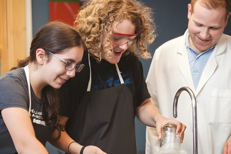 Tres personas trabajan juntas en un laboratorio de la St. George's School of Montreal con estanterías y equipos al fondo.