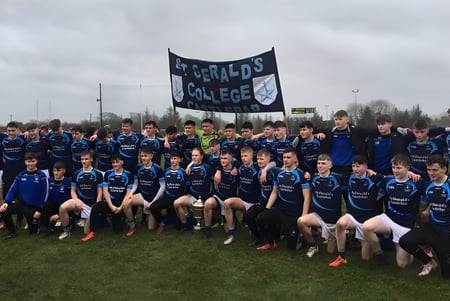 Un grupo de jóvenes atletas en uniformes azules posan en el campo de deportes del St. Gerald's College frente a una gran pancarta.