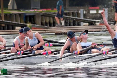 Un grupo de estudiantes de St. Hilda's Collegiate School rema en el agua frente a un muelle y edificios.
