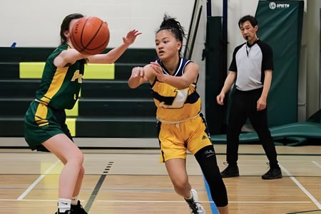 Dos jugadores de baloncesto en camisetas amarillas y verdes luchan por el balón en la cancha de St. James Collegiate.