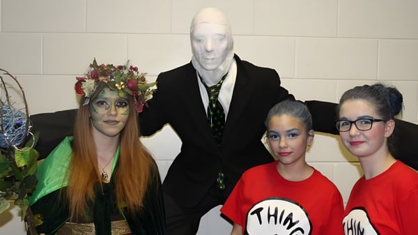 Tres estudiantes de la St. James' Regional High posan en coloridos y extravagantes disfraces frente a una pared de azulejos.
