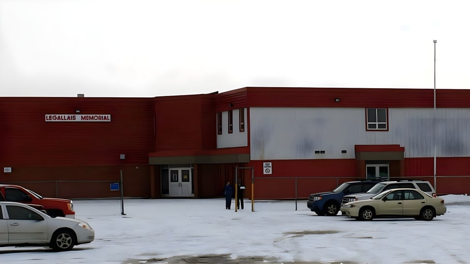 El edificio de ladrillo rojo de la St. James' Regional High se encuentra frente a un estacionamiento nevado con vehículos estacionados.