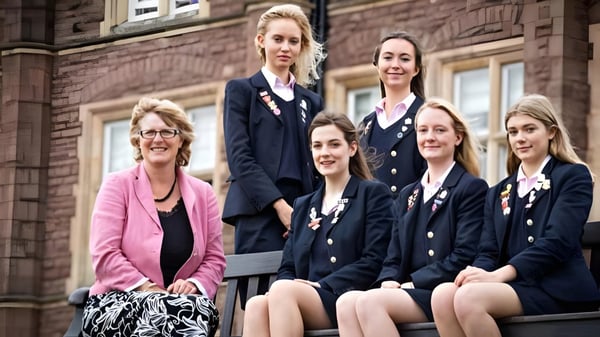 Un grupo de alumnas en uniformes escolares está frente a un edificio de ladrillo en el terreno de la St. James’ School.