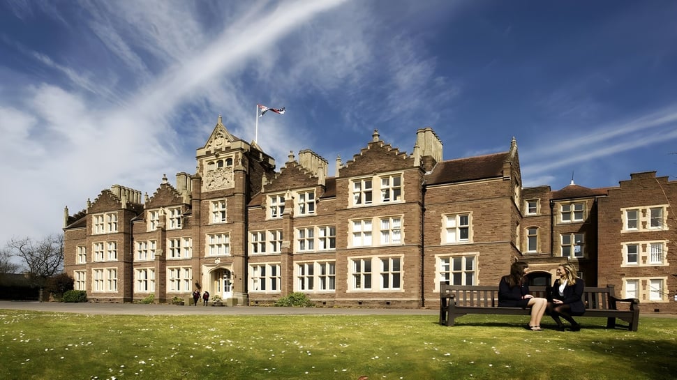 El histórico edificio de la St. James’ School se encuentra en un campo de hierba bajo un cielo azul.