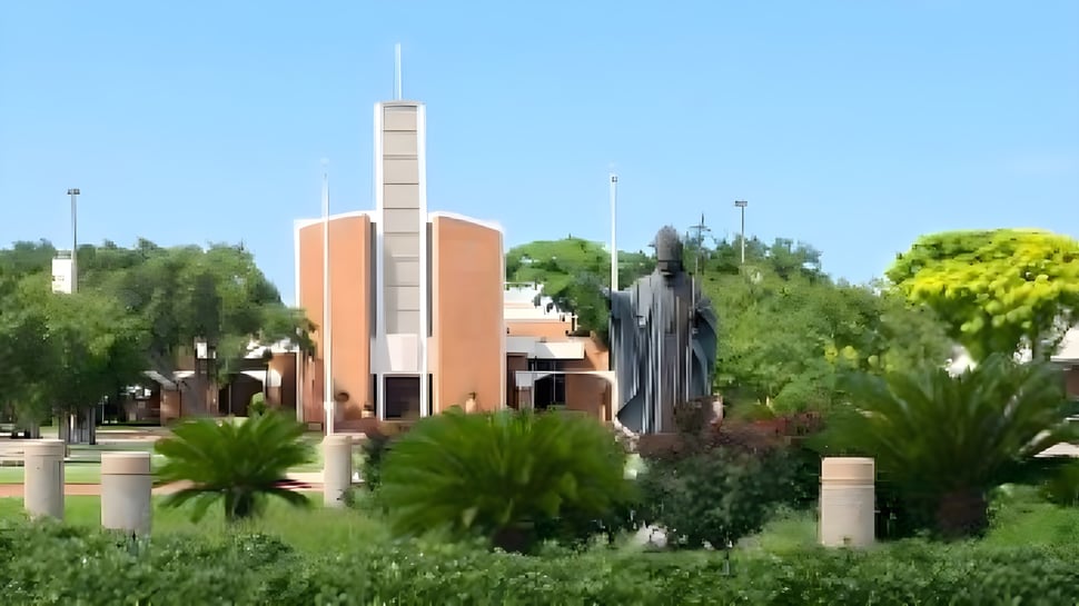 El moderno edificio de la St. John Paul II High School se encuentra con una alta torre en el verde con palmeras y otra vegetación.