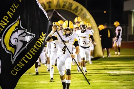 Estudiantes de la St. John Paul II High School entran al campo de fútbol con camisetas blancas.