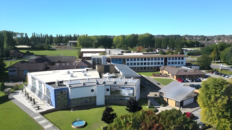 El extenso terreno del St. John Plessington Catholic College con edificios modernos y un entorno verde bajo un cielo despejado.