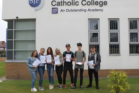 Un grupo de alumnas y alumnos se encuentra con certificados frente al edificio del St. John Plessington Catholic College.