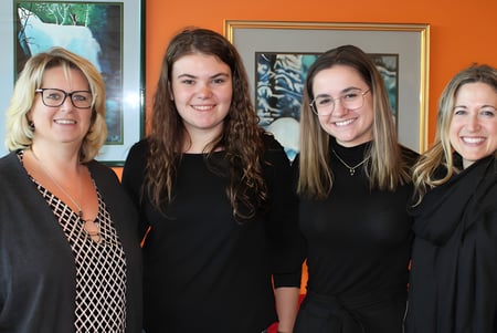 Cuatro mujeres posan frente a una pared naranja en el campus de la St. Johns High School.