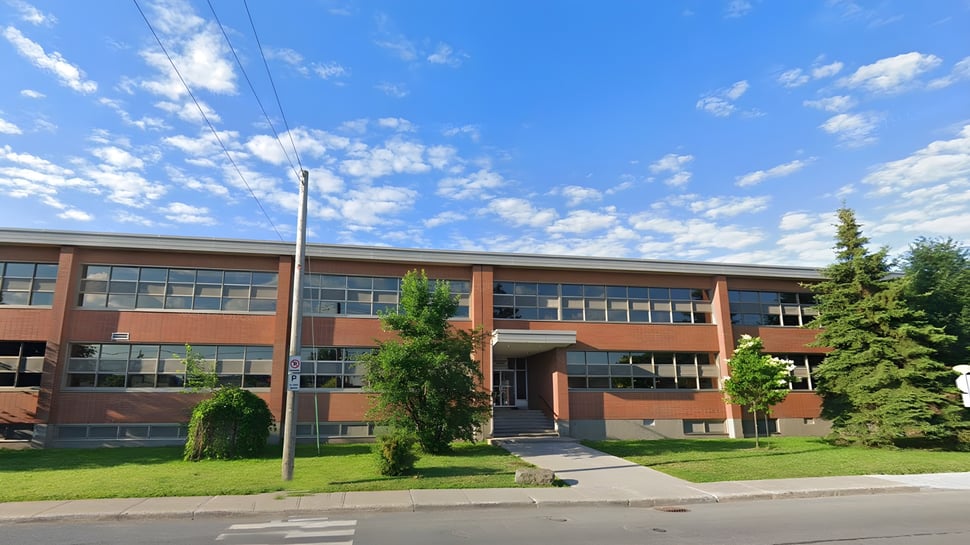 El edificio de ladrillo de varios pisos de la St. Johns High School se encuentra en un prado con árboles bajo un cielo azul.