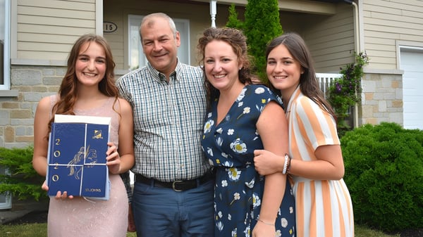 Una familia con dos adultos y dos jóvenes mujeres está frente a una casa residencial en el terreno de la St. Johns High School.