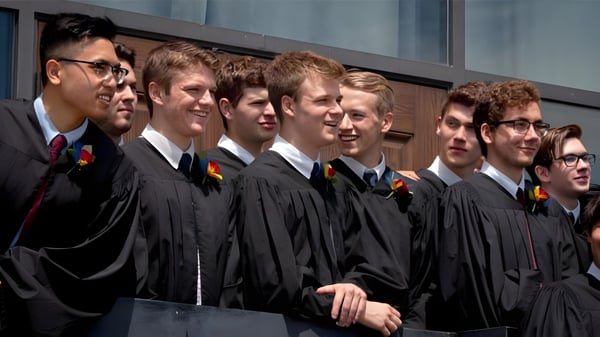 Un grupo de estudiantes de la St. John’s-Kilmarnock School está vestido con ropa de graduación frente a un edificio escolar.