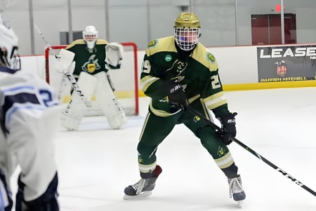 Un jugador de hockey de la St. John’s-Ravenscourt School está de pie con un uniforme verde y casco sobre el hielo.