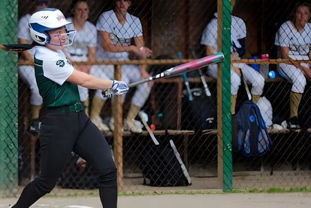 Un jugador de béisbol de la St. Johnsbury Academy batea en el plato durante un juego con espectadores en las gradas.