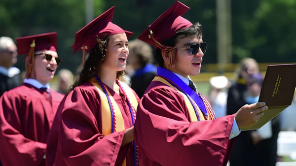 Un grupo de graduados de la St. Joseph High School está al aire libre con togas y birretes rojos sosteniendo sus diplomas.
