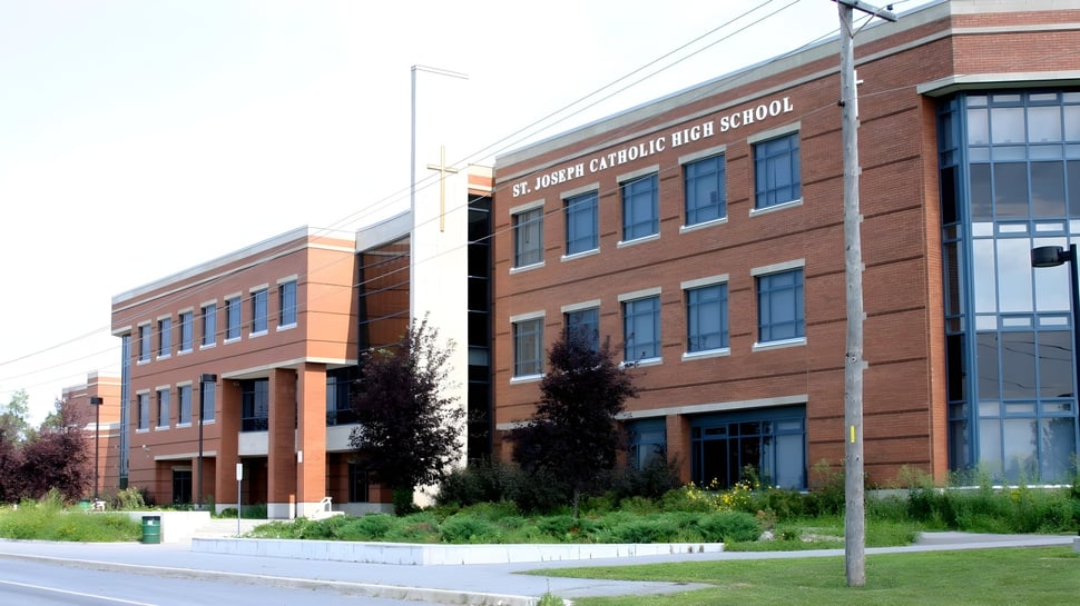 El edificio de ladrillo de varios pisos de la St. Joseph High School con grandes ventanas se encuentra en un terreno cubierto de hierba con árboles y una acera.